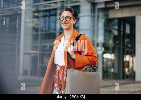 Reife Geschäftsfrau, die auf dem Weg zur Arbeit in der Stadt glücklich lächelt. Fröhliche Geschäftsfrau, die morgens zu Fuß in ihr Büro geht. Stockfoto