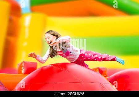 Glückliches kleines Mädchen mit viel Spaß auf einem aufgeblasen Burg beim Springen. Farbenfroher Spielplatz. Stockfoto