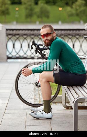 Ein Radfahrer sitzt auf einer Bank in einem Stadtpark, ruht sich aus, erholt sich während einer Radtour und radelt als Hobby. Stockfoto