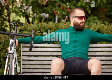 Ein Radfahrer sitzt auf einer Bank in einem Stadtpark, ruht sich aus, erholt sich während einer Radtour und radelt als Hobby. Stockfoto