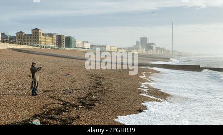 Farbbild eines Mannes am Brighton Beach in einem Mantel und einer flachen Mütze Stockfoto