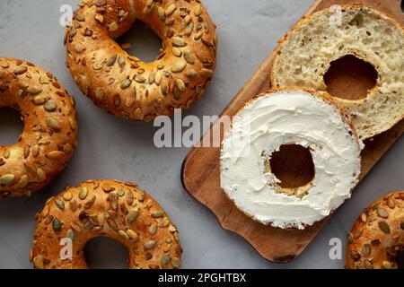 Hausgemachte Vollkorn-Bagel mit Frischkäse auf einem rustikalen Holzbrett, Draufsicht. Stockfoto