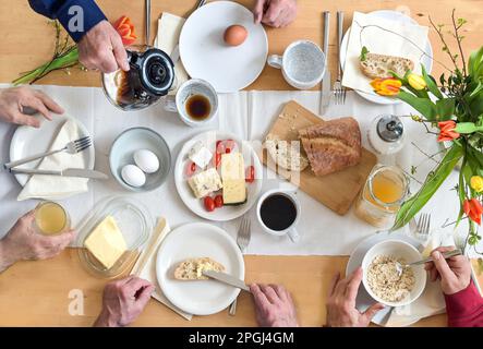 Gruppe von Personen, die gemeinsam auf einem Holztisch mit Brot, Käseeiern und Kaffee frühstücken, Blick von oben, ausgewählter Fokus Stockfoto
