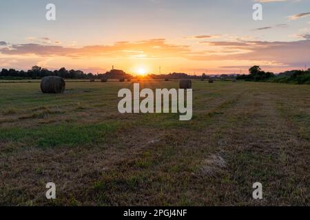 Runde Heuballen auf dem Feld bei goldenem Sonnenuntergang, Sonnenuntergang auf dem Land mit bunten Wolken Stockfoto