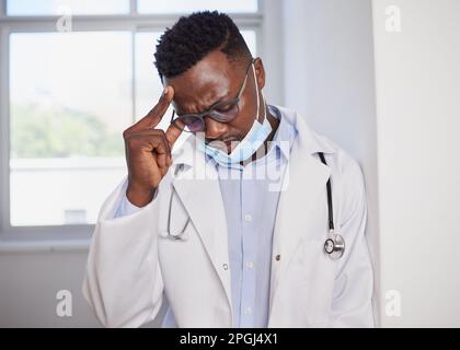 Schwarzer Arzt sieht verärgert nach der Operation mit medizinischer Maske, gestresst Stockfoto