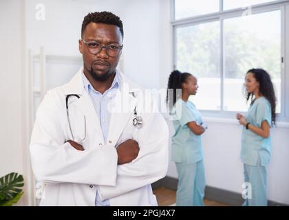 Porträt eines schweren Arztes mit gefalteten Armen, mit zwei Krankenschwestern im Hintergrund Stockfoto