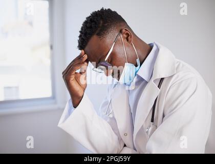 Schwarzer Arzt sieht verärgert nach der Operation mit medizinischer Maske, gestresst Stockfoto