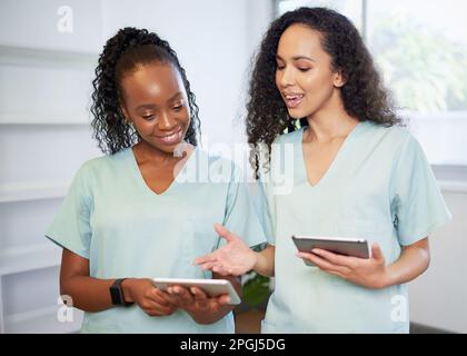 Zwei junge Frauen im medizinischen Bereich, die Peelings tragen, diskutieren mit digitalen Tablets Stockfoto