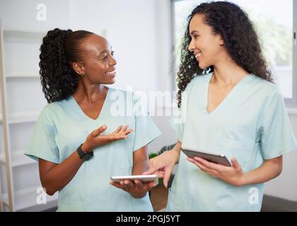 Zwei junge Frauen im medizinischen Bereich, die Peelings tragen, diskutieren mit digitalen Tablets Stockfoto