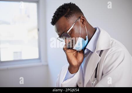 Schwarzer Arzt sieht verärgert nach der Operation mit medizinischer Maske, gestresst Stockfoto