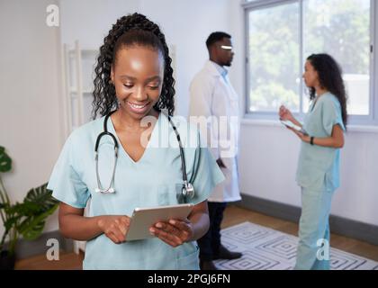 Eine Ärztin in Peelings verwendet ein digitales Tablet mit einem medizinischen Team im Hintergrund Stockfoto