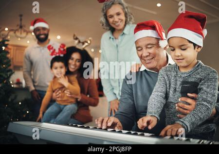 Klavier, weihnachten und älterer Mann mit Enkel im Wohnzimmer, glücklich und feierlich, während sie sich in ihrem Zuhause verbinden. Familie, Musik und Rentner Stockfoto