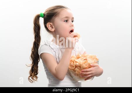 Ein Mädchen nimmt Chips Snacks mit Schmalz aus einer Schüssel und isst sie, Porträt auf weißem Hintergrund und Kopierraum, ungesunde und ungesunde Nahrung. Stockfoto