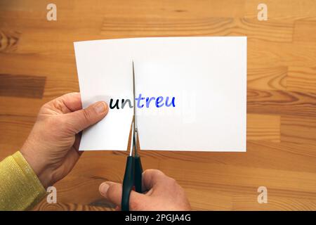Ein Wort auf einem Papier, die Negation "un" ist abgeschnitten, untreu - treu, untreu - treu Stockfoto