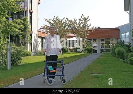 Seniorin, die mit einem Rollator im Außenbereich des Seniorenwohnsitzes läuft, Vorderansicht Stockfoto