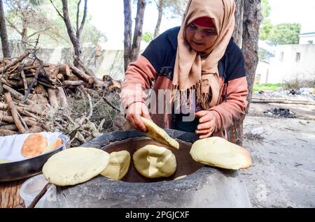 Tunis, Tunesien. 22. März 2023. Tunis, Tunesien, 22. März 2023. Eine tunesische Frau backt das Tabouna-Brot in einem traditionellen Tonofen, bevor sie es auf einem Markt in Tunis verkauft. Tabouna ist ein altes tunesisches Brot aus Weizen-, Grieß- oder Gerstenmehl, das an den Wänden eines traditionellen Terrakotta-Ofens gekocht wird. Tabouna ist besonders beliebt während des heiligen muslimischen Monats Ramadan (Kreditbild: © Hasan mrad/IMAGESLIVE via ZUMA Press Wire). Nicht für den kommerziellen GEBRAUCH! Stockfoto