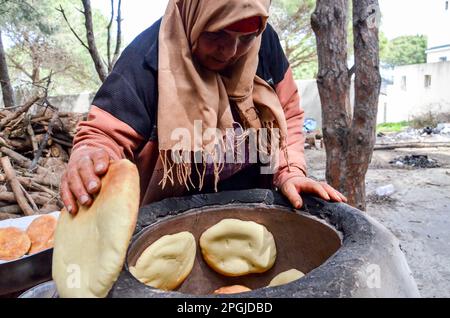 Tunis, Tunesien. 22. März 2023. Tunis, Tunesien, 22. März 2023. Eine tunesische Frau backt das Tabouna-Brot in einem traditionellen Tonofen, bevor sie es auf einem Markt in Tunis verkauft. Tabouna ist ein altes tunesisches Brot aus Weizen-, Grieß- oder Gerstenmehl, das an den Wänden eines traditionellen Terrakotta-Ofens gekocht wird. Tabouna ist besonders beliebt während des heiligen muslimischen Monats Ramadan (Kreditbild: © Hasan mrad/IMAGESLIVE via ZUMA Press Wire). Nicht für den kommerziellen GEBRAUCH! Stockfoto