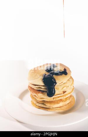 Pfannkuchen, gestapelt auf einem weißen Teller, werden mit Schokolade gekrönt. Stockfoto