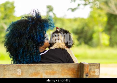 Goiania, Goias, Brasilien – 20. März 2023: Foto einer jungen Frau von hinten, die mit einem Hündchen auf einer Bank sitzt. Stockfoto