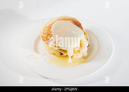 Pfannkuchen auf einem weißen Teller gestapelt, werden Pfannkuchen mit gesüßter Kondensmilch gekrönt. Stockfoto