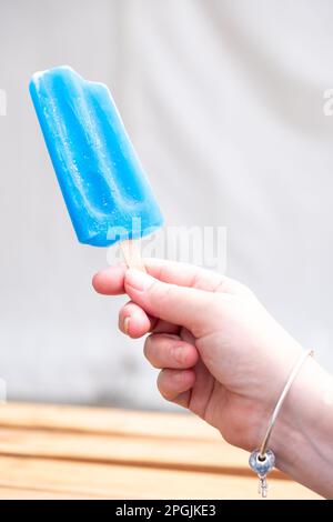 Eine Frauenhand, die ein teilweise knabbeltes blaues Eis auf einer Dorffestzeit hält. Stockfoto