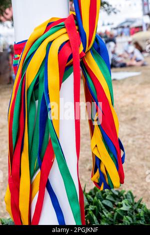 Farbenfrohe Bänder, die auf einer Dorffeier um den Fuß einer traditionellen englischen Maypole gebunden sind. Stockfoto