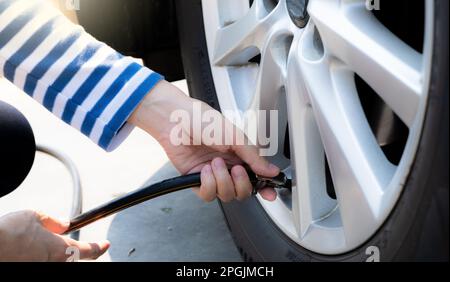 Frau bläst den Reifen auf. Frau, die den Reifendruck überprüft und Luft in den Reifen des Autorads pumpt. Autowartung zur Sicherheit vor der Reise. Stockfoto