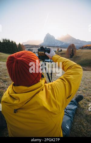 Eine vertikale Rückansicht eines professionellen Fotografen, der Fotos von einem Berg auf einem Stativ macht Stockfoto