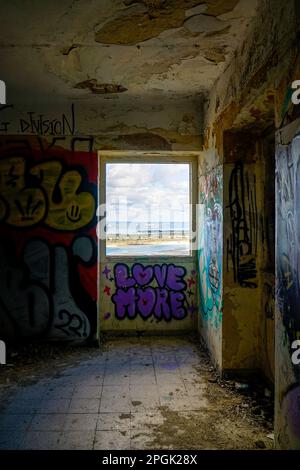 Blick auf Tróia durch ein Fenster mit einer verlassenen Festung in der Serra da Arrabida in Setubal, wo die Wände mit Graffiti bedeckt sind. Stockfoto