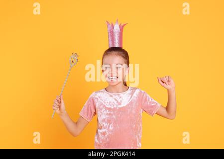 Süßes Mädchen in rosa Krone mit Zauberstab auf gelbem Hintergrund. Kleine Prinzessin Stockfoto