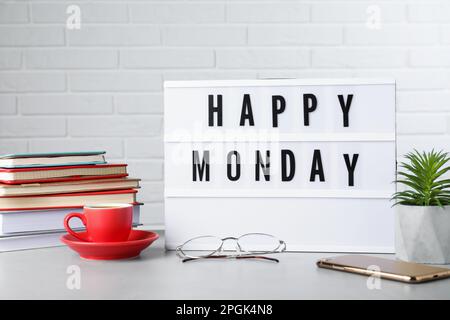 Lichtbox mit Nachricht „Happy Monday“, Büropapier und eine Tasse Kaffee auf dem Schreibtisch Stockfoto