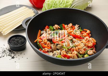 Gebratene Nudeln mit Pilzen, Garnelen und Gemüse im Wok auf einem weißen Holztisch umrühren Stockfoto