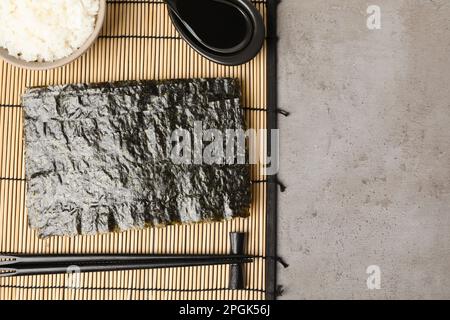 Trocknen Sie Nori-Blätter, Reis, Sojasauce und Essstäbchen auf einem grauen Tisch, flach liegen. Platz für Text Stockfoto