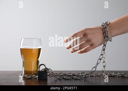 Frau an ein Glas Bier gekettet am Tisch vor weißem Hintergrund, Nahaufnahme. Alkoholsucht Stockfoto