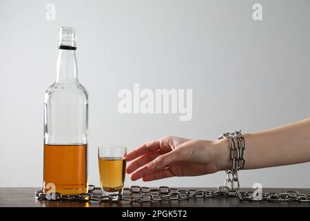 Süchtig werdende Frau an eine Flasche alkoholisches Getränk gekettet am Holztisch vor weißem Hintergrund, Nahaufnahme Stockfoto