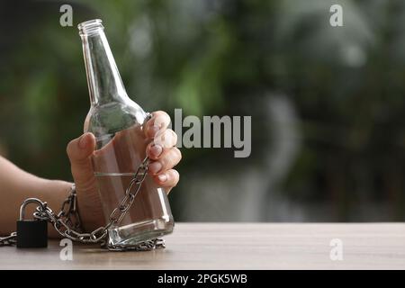 Mann an eine Flasche Wodka am Tisch gekettet vor unscharfem Hintergrund, Nahaufnahme mit Platz für Text. Alkoholsucht Stockfoto