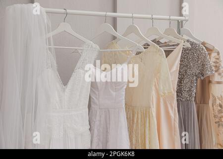 Kleiderbügel mit verschiedenen schönen Kleidern und Hochzeitsschleier auf dem Regal im Atelier Stockfoto