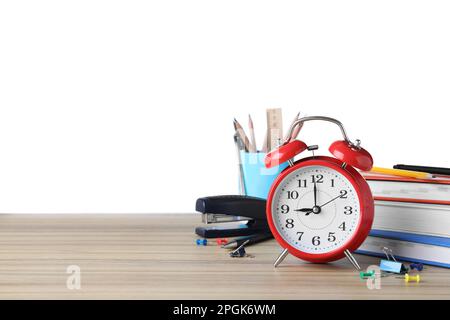 Roter Wecker und verschiedene Schreibwaren auf Holztisch vor weißem Hintergrund, Platz für Text. Zeit für die Schule Stockfoto