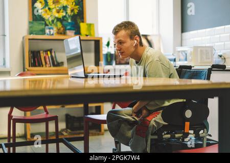 Gut aussehender junger behinderter Mann, der in einem Kätzchen mit dem Handy spricht. Menschen mit Behinderungen Stockfoto