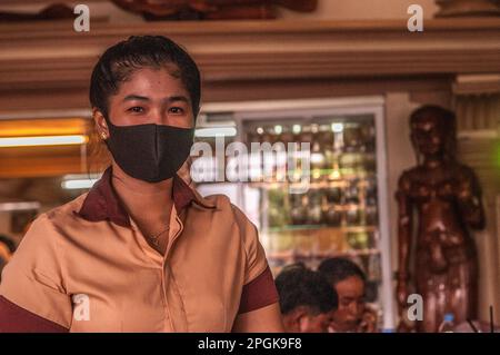 Porträt einer kambodschanischen Kellnerin, die eine Gesichtsschutzmaske trägt, in einem Restaurant während der COVID-Pandemie, Kampong Cham Stadt, Kambodscha. © Kraig Stockfoto