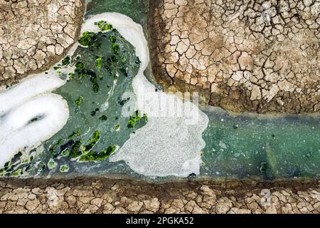 Ansicht von oben: Abwasser mit Luftblasen und Moos, das durch einen gerissenen Graben fließt. Sauerstoffblase in der Schmutzwasseraufbereitung in einem wassergefüllten Graben Stockfoto