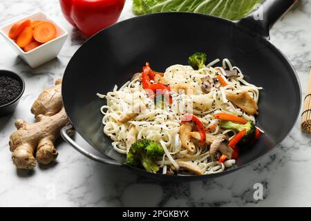 Gebratene Nudeln mit Huhn und Gemüse im Wok auf einem weißen Marmortisch umrühren Stockfoto