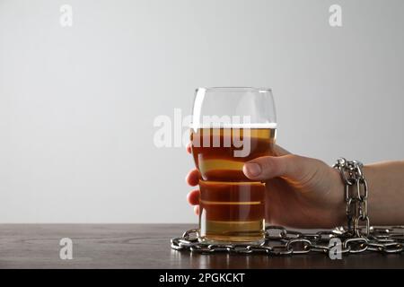 Frau mit angeketteter Hand und einem Glas Bier am Holztisch vor weißem Hintergrund, Nahaufnahme. Alkoholsucht Stockfoto