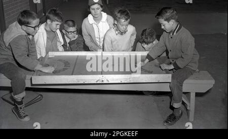 1950er, historisch, draußen, Jungs beobachten zwei Jugendliche, die auf einer langen Holzbank sitzen und ein Brettspiel spielen, Paddle Pool, USA. Stockfoto