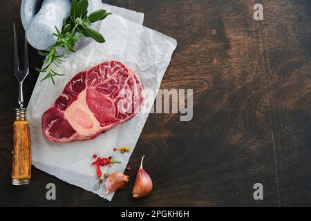 Rohes Steak-Fleisch von Osso Buco. Barbecue-Fleisch. Rohe, frische, kreuzgeschnittene Kalbsschenkel und Gewürze Pfeffer, Rosmarin, Thymian und Salz auf altem Holzhintergrund. Rindfleisch Stockfoto