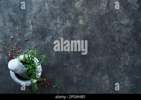 Hintergrund der Kochkunst. Grüne Rosmarin-Äste, Olivenöl, Knoblauch, Pfefferkörner und heiße Paprika auf dunklem Betontisch. Lebensmittelzutaten Top vi Stockfoto