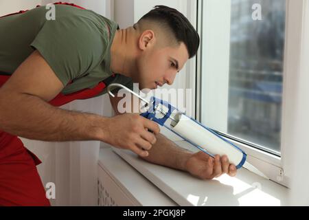 Bauarbeiter versiegelt Fenster mit Versiegelung in Innenräumen Stockfoto