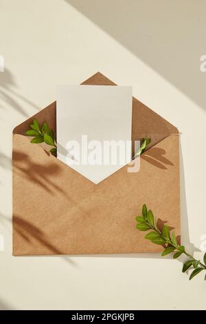 Offener Umschlag Schreibwaren Karte Mockup Einladung, leere Grußkarte und grüne Blätter unter Schatten - minimale Komposition. Platz für Text. Stockfoto