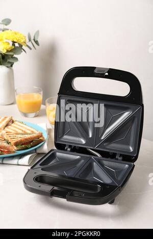 Moderne Grillmaschine und Sandwiches auf weißem Tisch Stockfoto