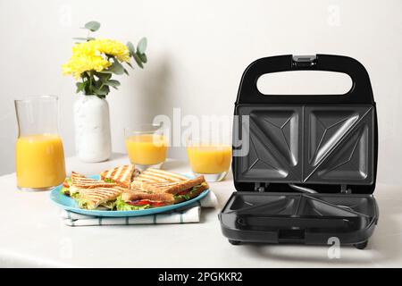 Moderne Grillmaschine und Sandwiches auf weißem Tisch Stockfoto